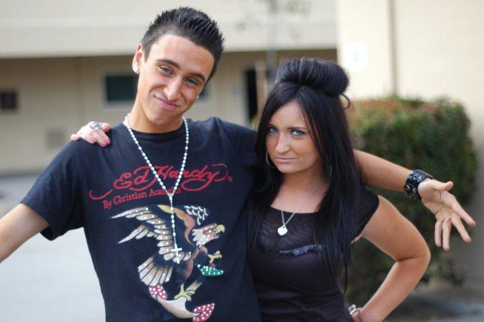 A young man in an Ed Hardy T-shirt poses with a woman with teased black hair.