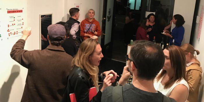 Guests at a crowded party sticker a wall chart headed "Rate this ridiculous cannabis brand."