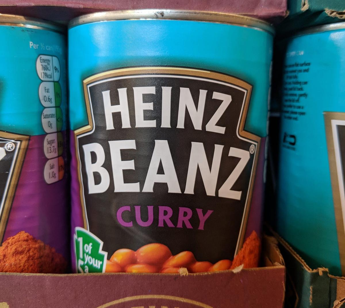 Cans of "Heinz Beanz Curry" on a shelf.