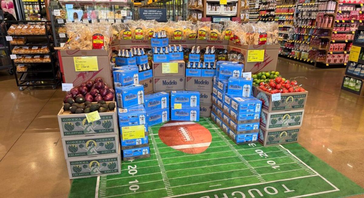 A grocery store display of Modelo beer cases and tortilla chips stacked on a football-field floor graphic reading "Touchdown."