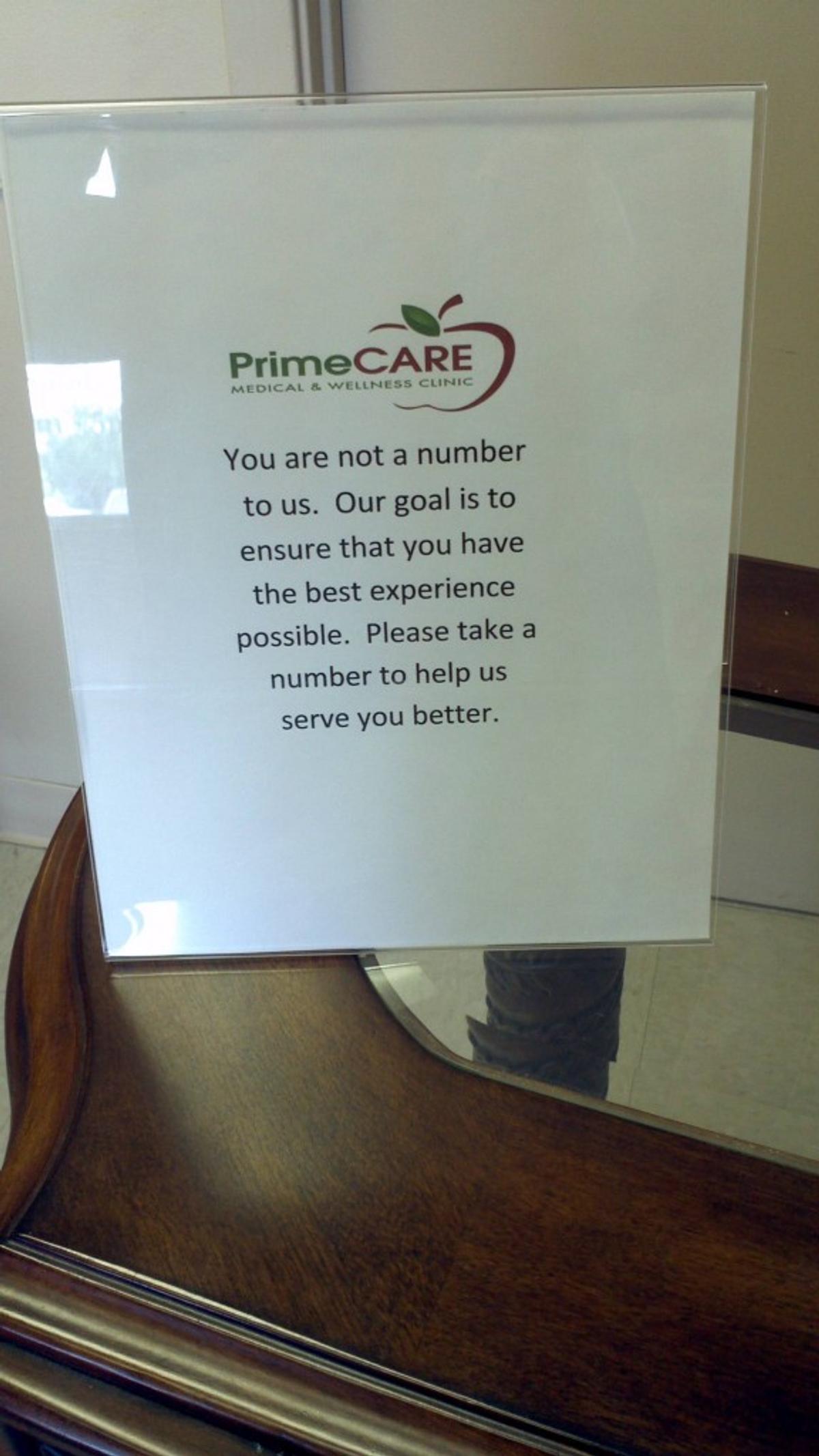 A PrimeCARE clinic sign reading "You are not a number to us... Please take a number to help us serve you better."