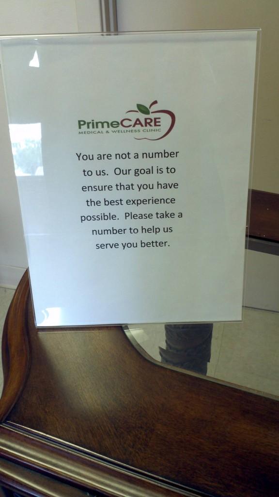 A PrimeCARE clinic sign reading "You are not a number to us... Please take a number to help us serve you better."