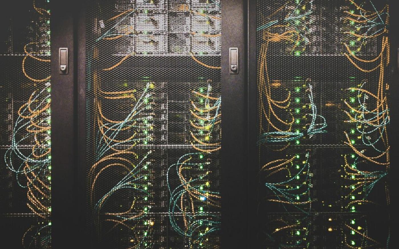 Server racks threaded with orange and teal fibre, status lights along each row