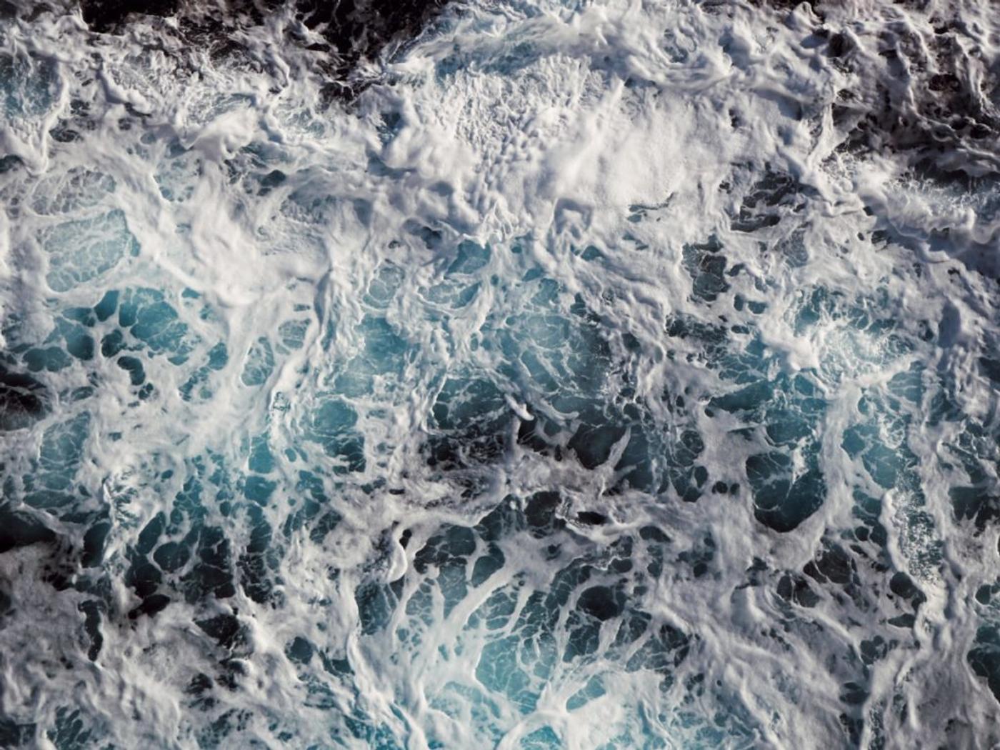 Churning white sea foam over deep blue water, seen from directly above