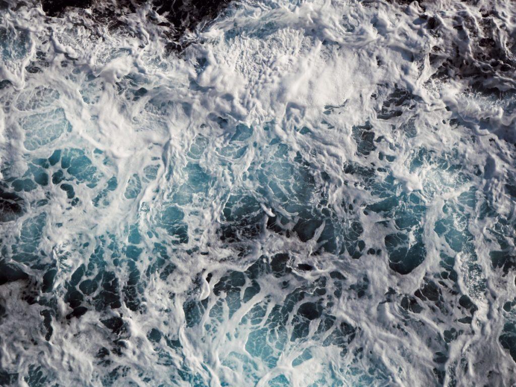Churning white sea foam over deep blue water, seen from directly above