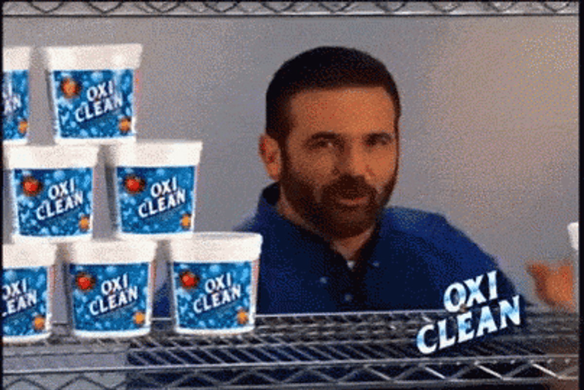 Billy Mays beside a shelf stacked with tubs of OxiClean in an infomercial still.
