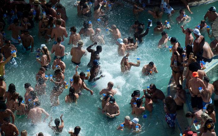 A packed hotel pool, dozens of people standing shoulder to shoulder in the water holding plastic cups.