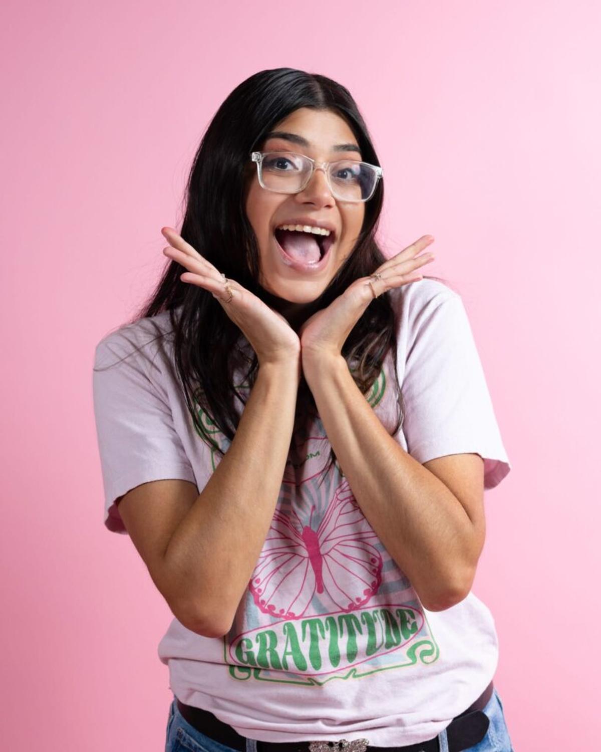 Esther Fernandez, hands raised by her face in delight, wears a butterfly T-shirt reading "Gratitude."