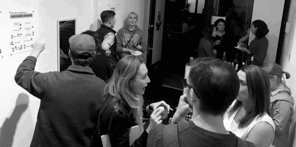 Guests at a party placing stickers on a wall poster headed "rate the ridiculous... cannabis brand."