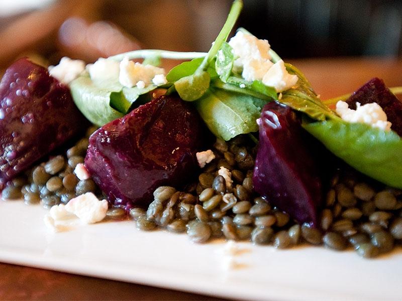 Roasted beet chunks, lentils, greens, and crumbled cheese on a white plate.