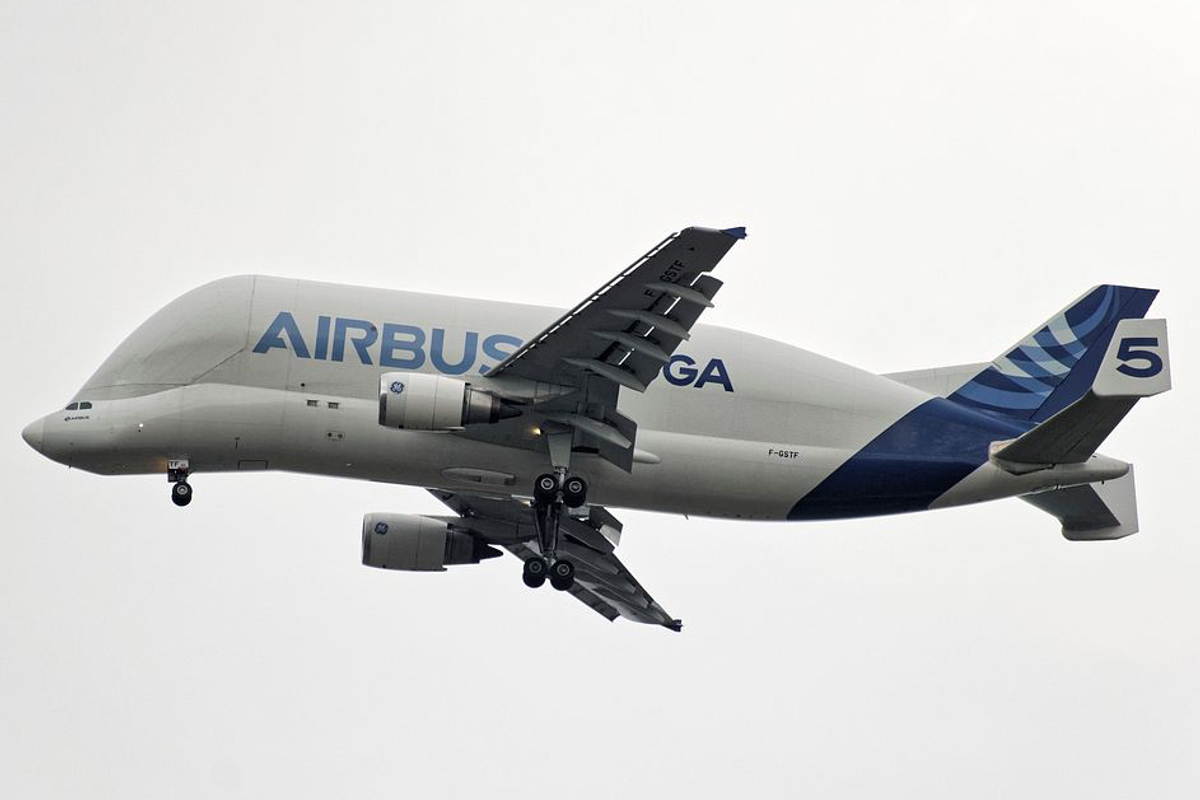 An Airbus Beluga cargo plane in flight, "AIRBUS" lettered along its bulbous white fuselage.