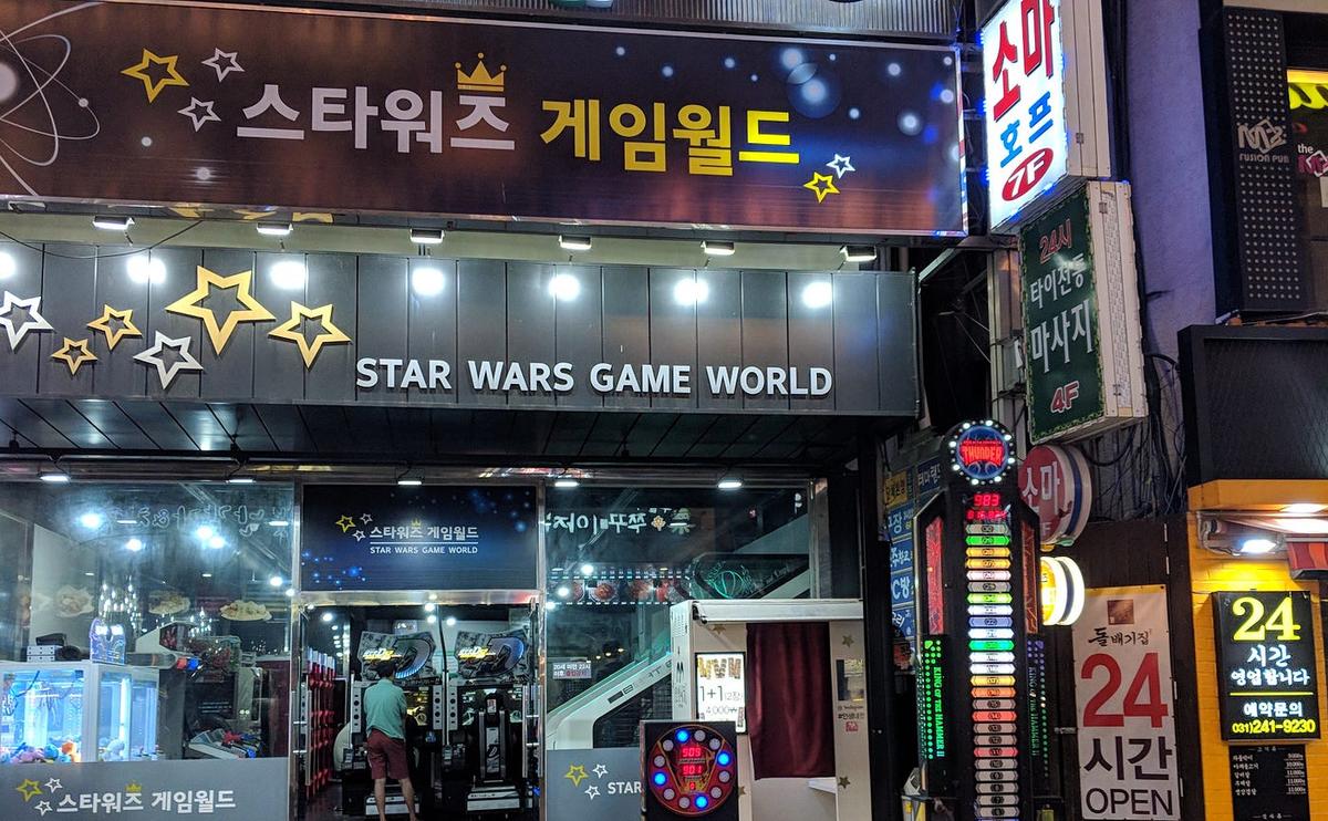 Neon arcade storefront signed "STAR WARS GAME WORLD" in English and Korean, surrounded by stars.