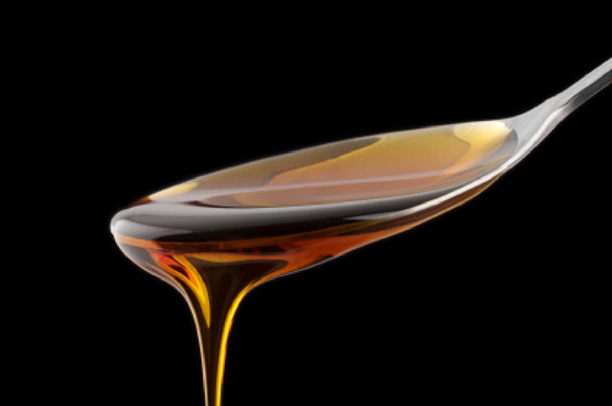 Amber syrup dripping off a spoon against a black background.