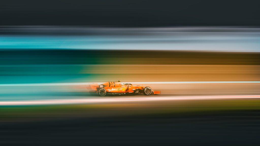 A red Formula 1 car numbered 16 blurring past in streaks of teal and orange.