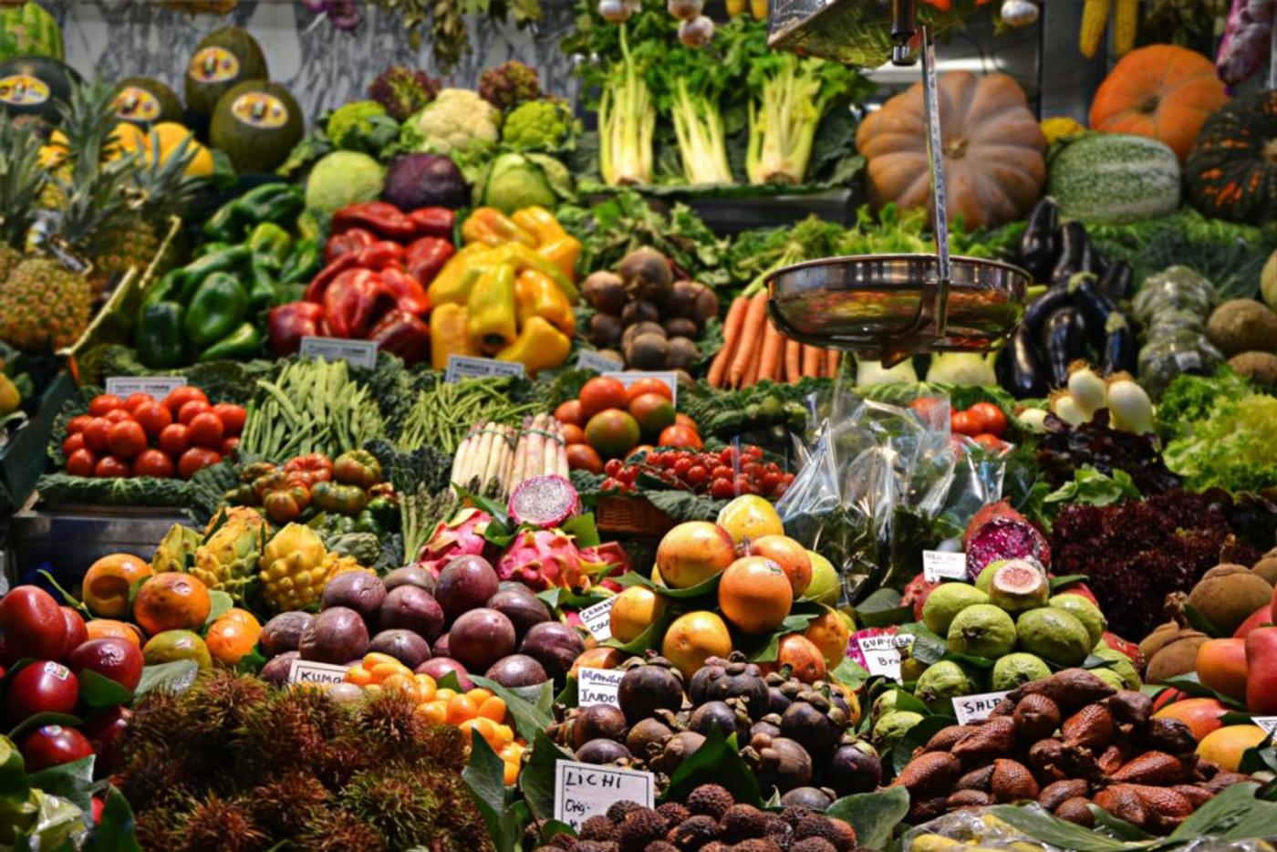 A market stall banked with fruit and vegetables, hand-lettered price cards among them