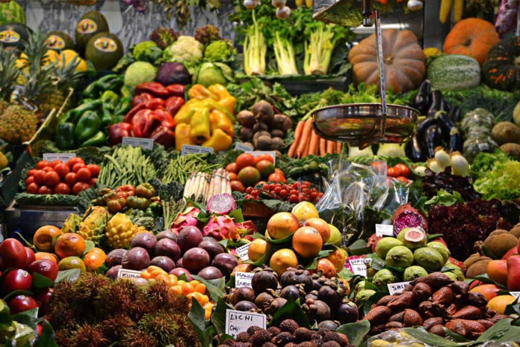 A market stall banked with fruit and vegetables, hand-lettered price cards among them
