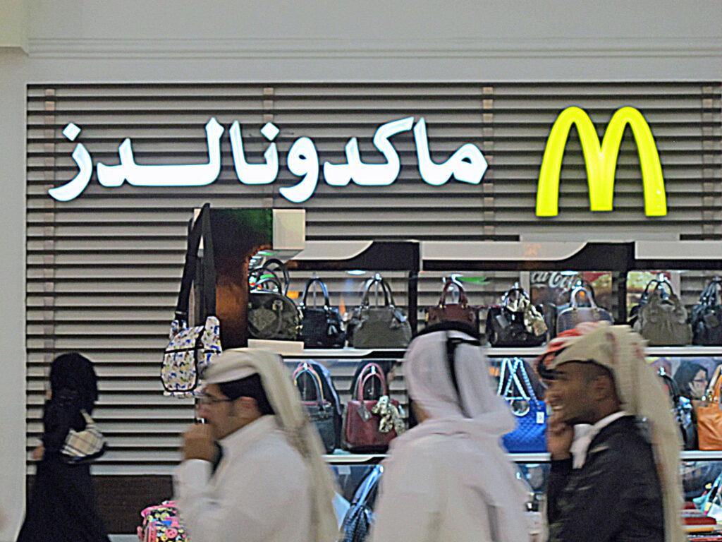 McDonald's golden arches beside the brand name in Arabic script, above a mall handbag display.