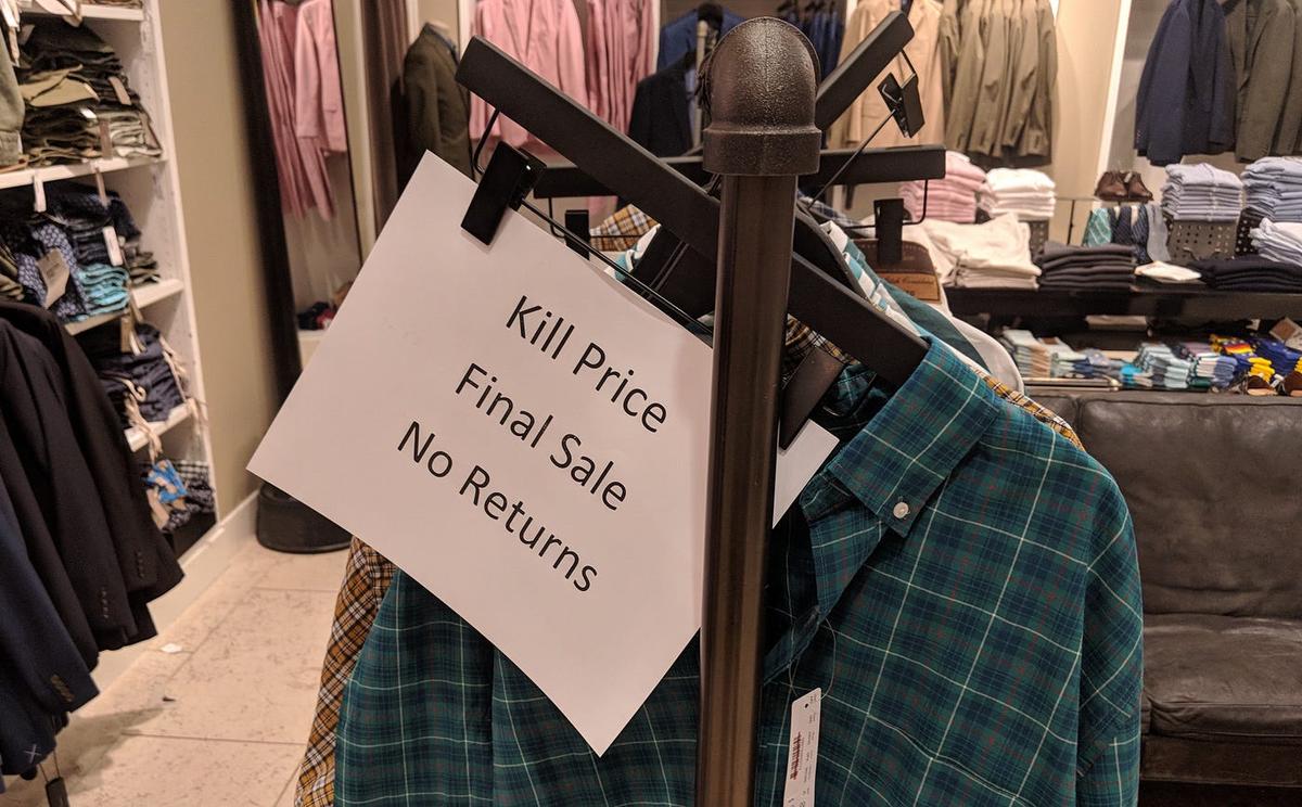 A printed sign clipped to a clothing rack in a menswear store reads "Kill Price / Final Sale / No Returns."
