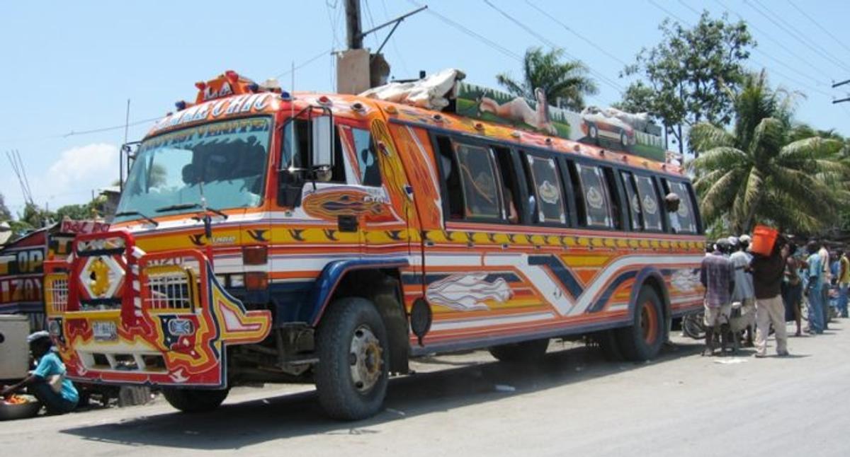 A brightly painted Haitian tap tap bus decorated in red, orange, and blue, parked by a roadside.