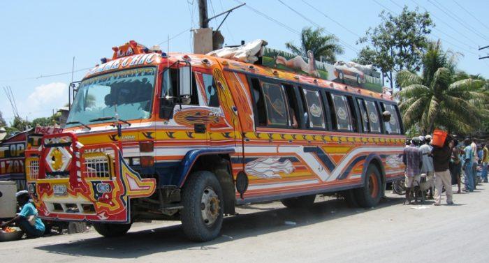 A brightly painted Haitian tap tap bus decorated in red, orange, and blue, parked by a roadside.