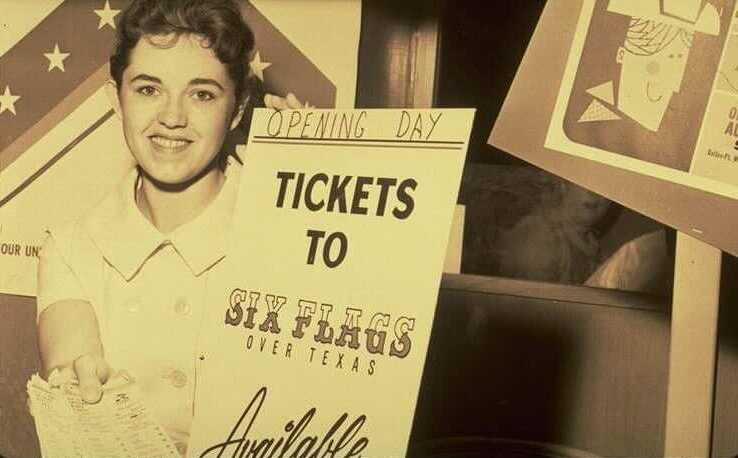 A vintage photo of a woman holding a sign reading "Opening Day tickets to Six Flags Over Texas available."