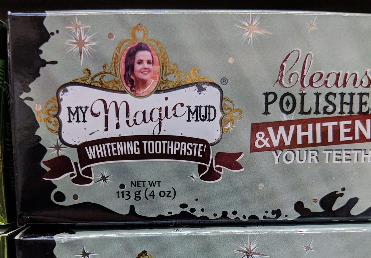 Toothpaste box reading "My Magic Mud Whitening Toothpaste," with a woman's portrait in a gold oval frame.