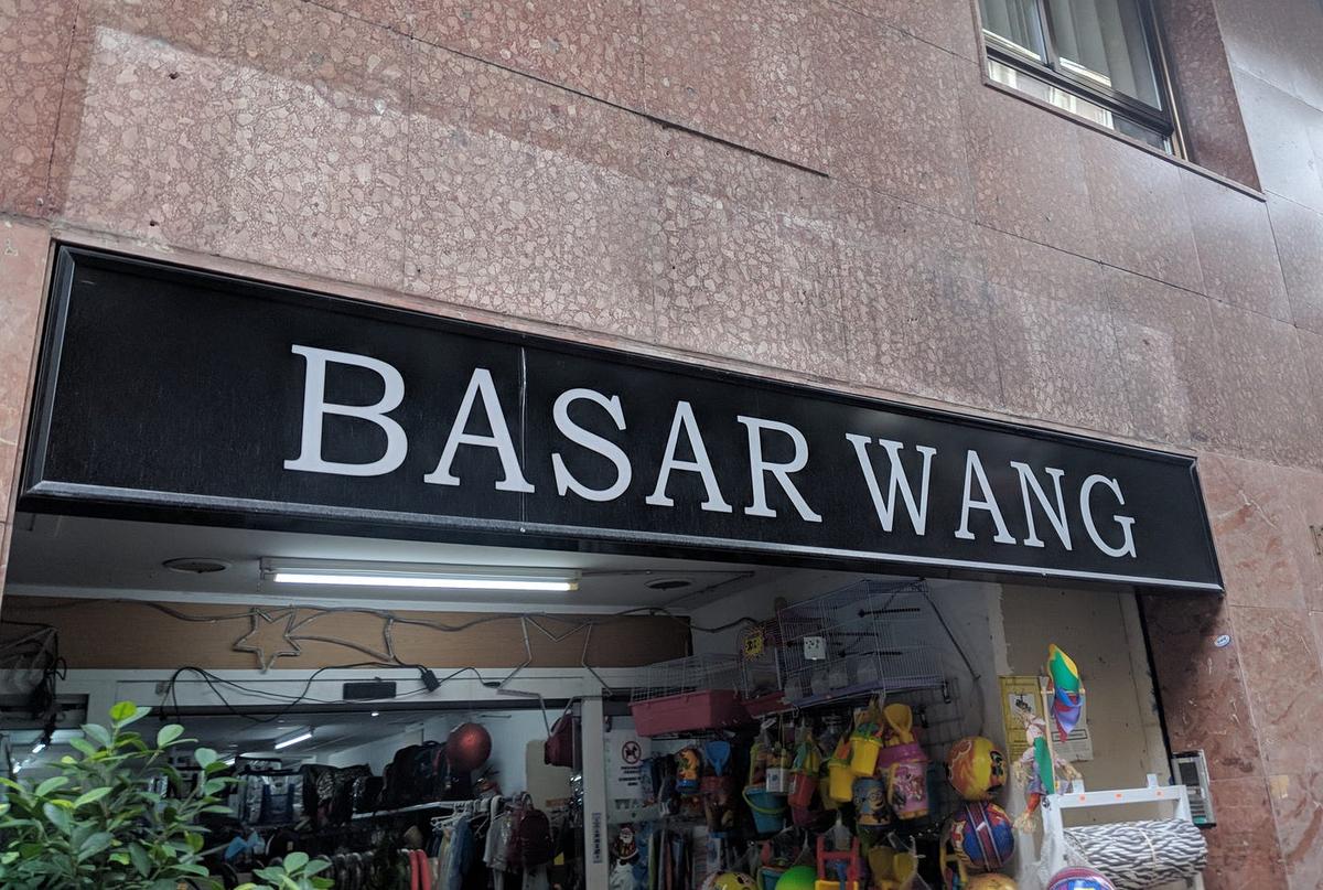 A black shop sign reading "Basar Wang" above a store crammed with birdcages, buckets and toys.