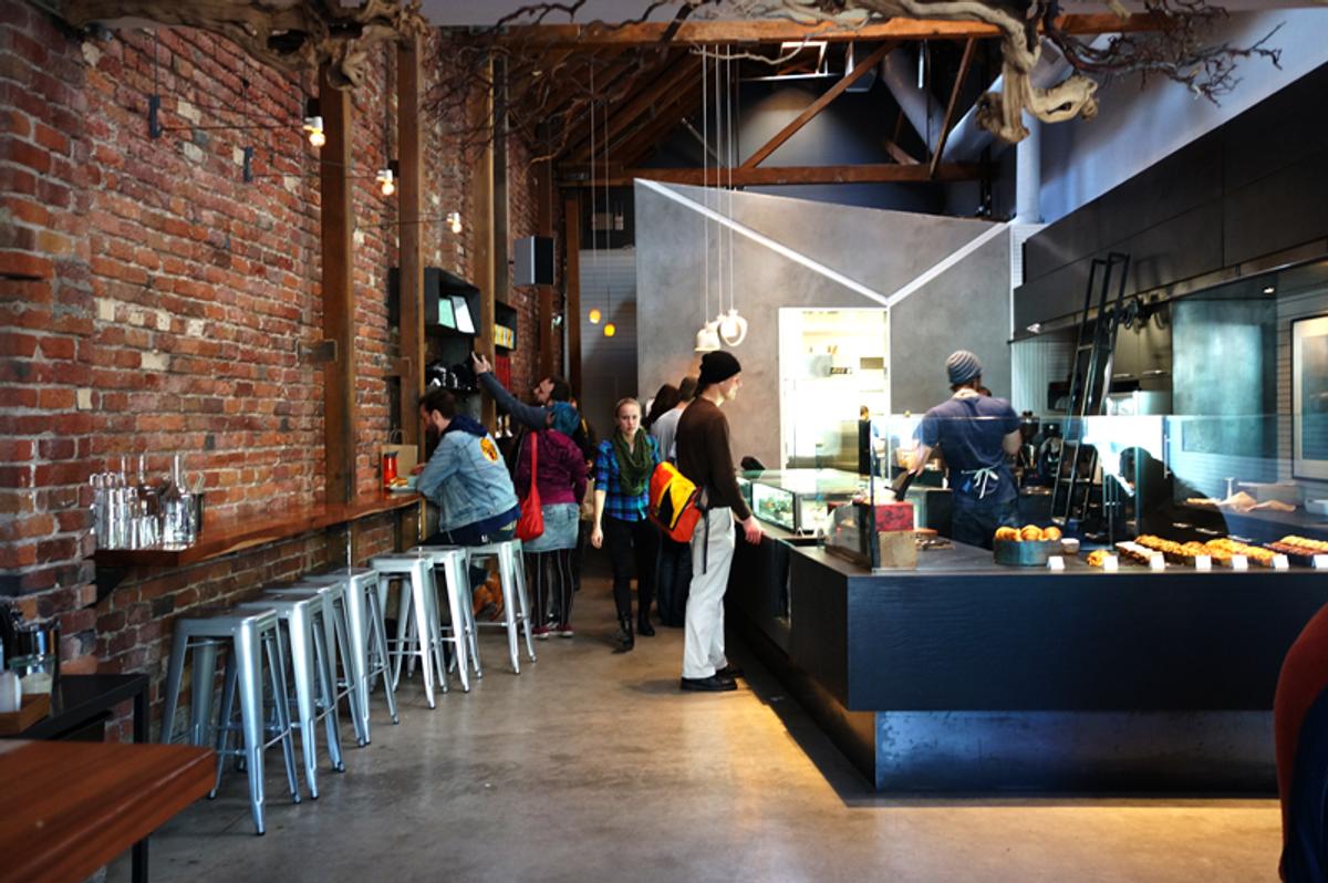 Customers at the counter of Craftsman and Wolves, a cafe with exposed brick, timber beams, and metal stools.