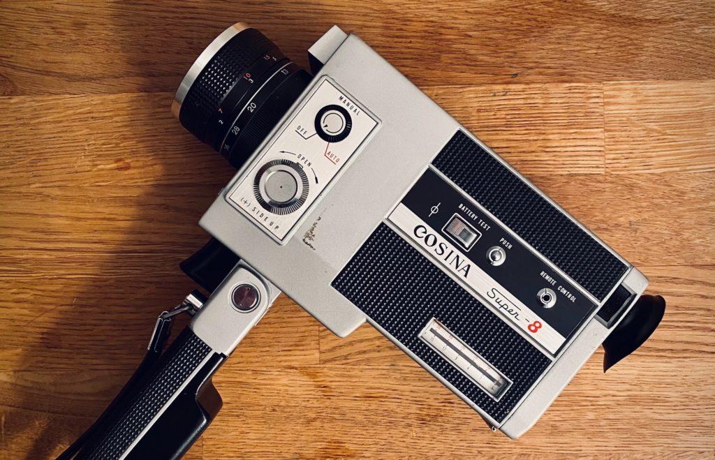 A vintage Cosina Super-8 movie camera on a wooden floor, badged "Cosina Super-8."
