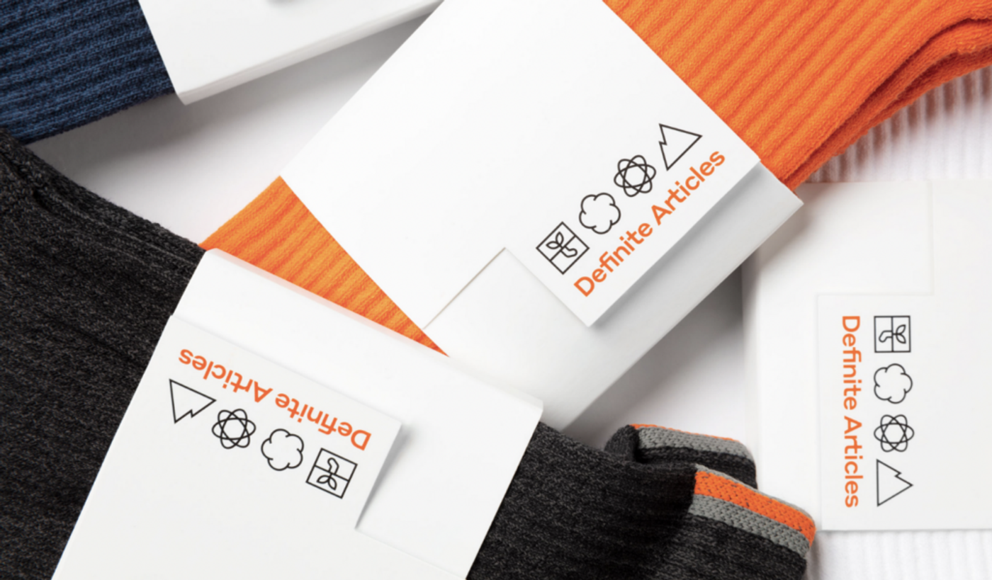 Definite Articles labels on folded socks in orange, charcoal and navy