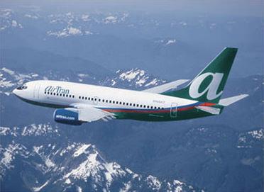 An AirTran jet flying above snow-capped mountains.