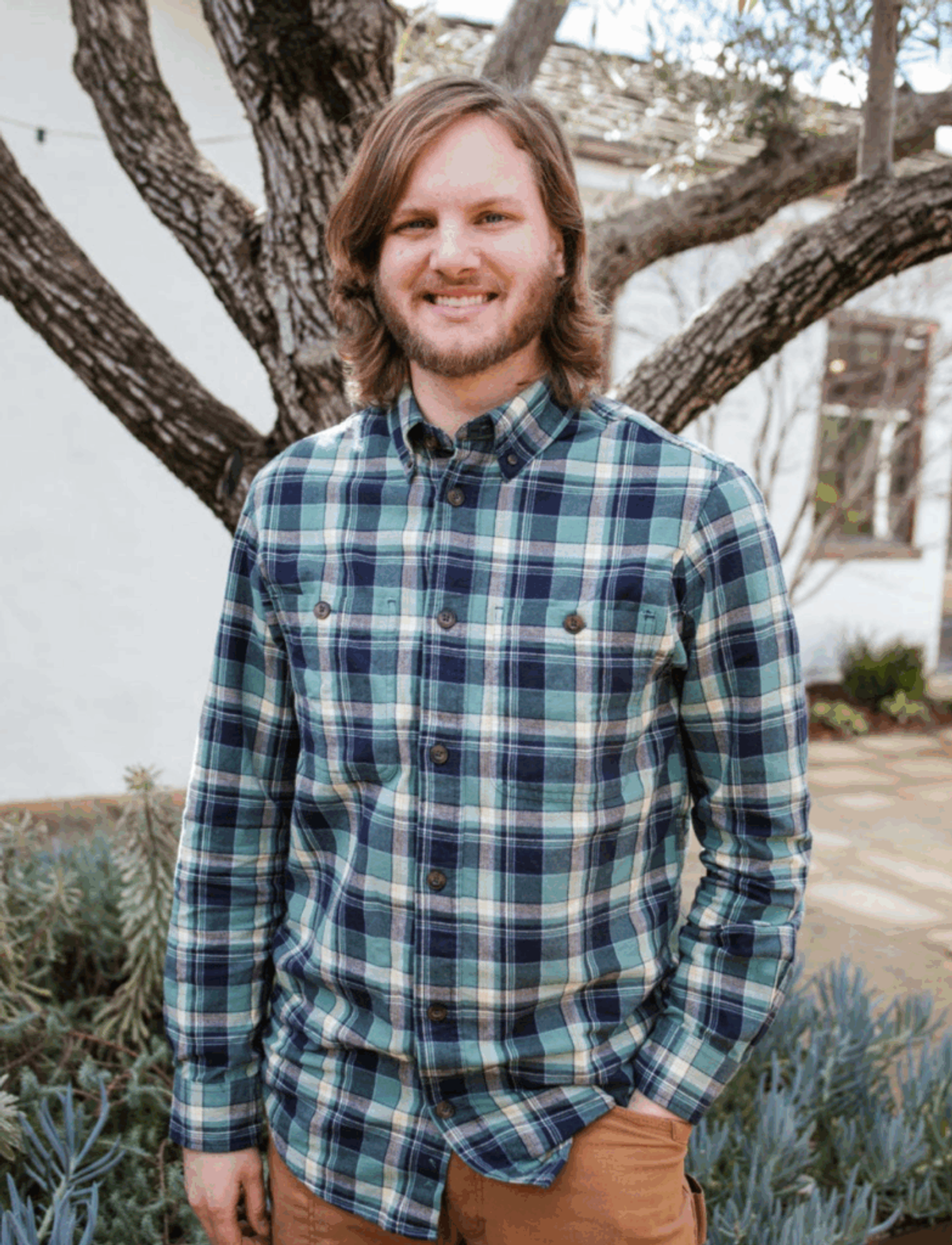 Carl Formaker, in a green and navy plaid shirt, smiling in front of a bare tree.