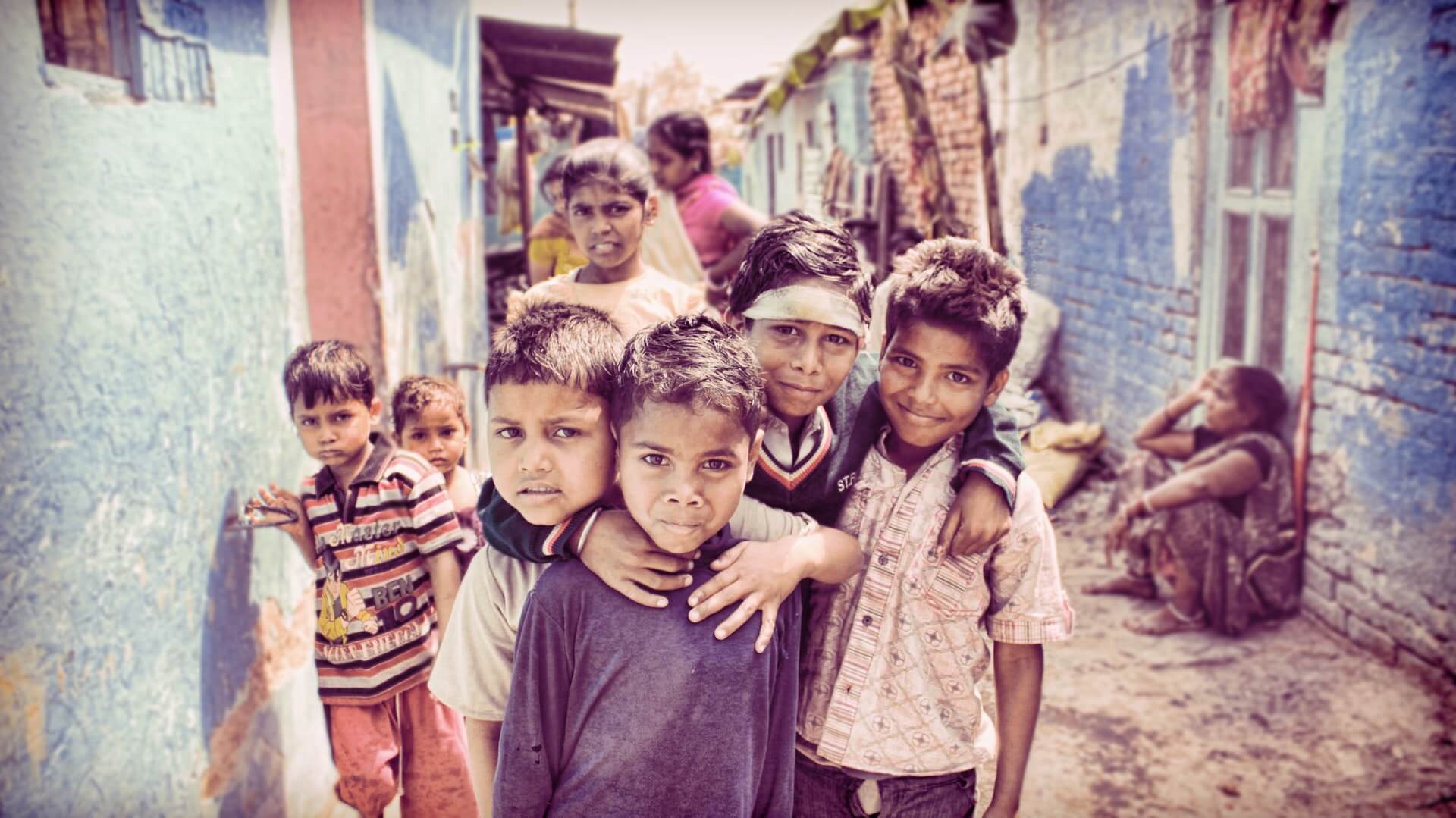 A group of children standing together in a narrow lane between painted houses.