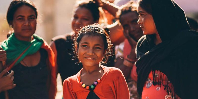 A girl smiling among women and children in a rural Indian community at golden hour.