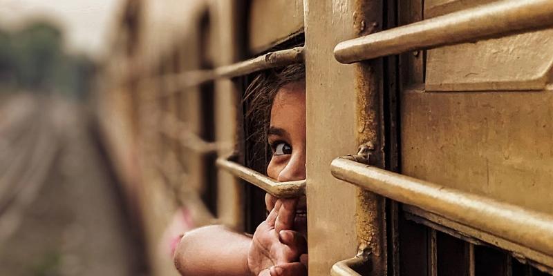 A child looking out through the bars of a train window.