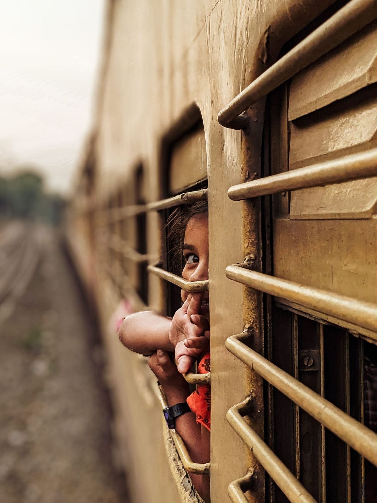 A child looking out through the bars of a train window.
