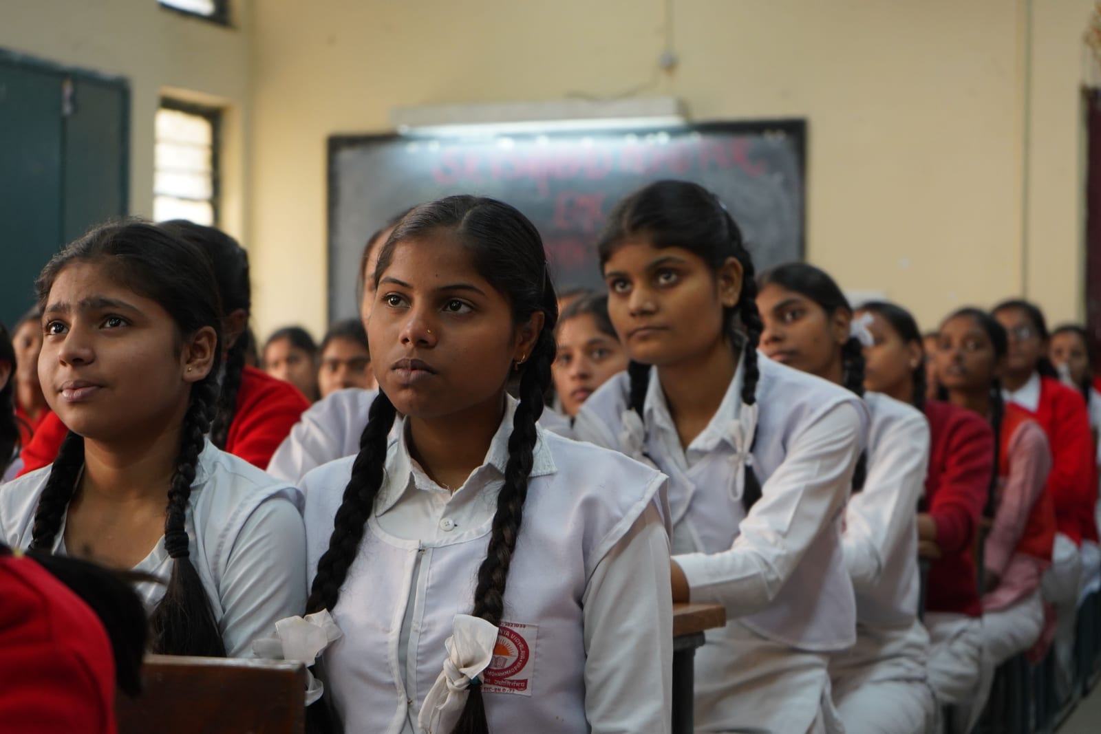 Schoolgirls in white uniforms listening in a classroom.