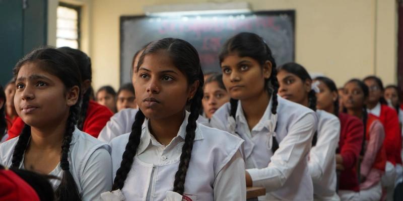 Schoolgirls in white uniforms listening in a classroom.