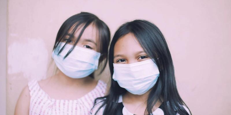 Two girls wearing face masks, looking at the camera.
