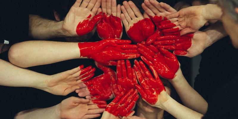 Several pairs of hands together around a heart painted in red across their palms.