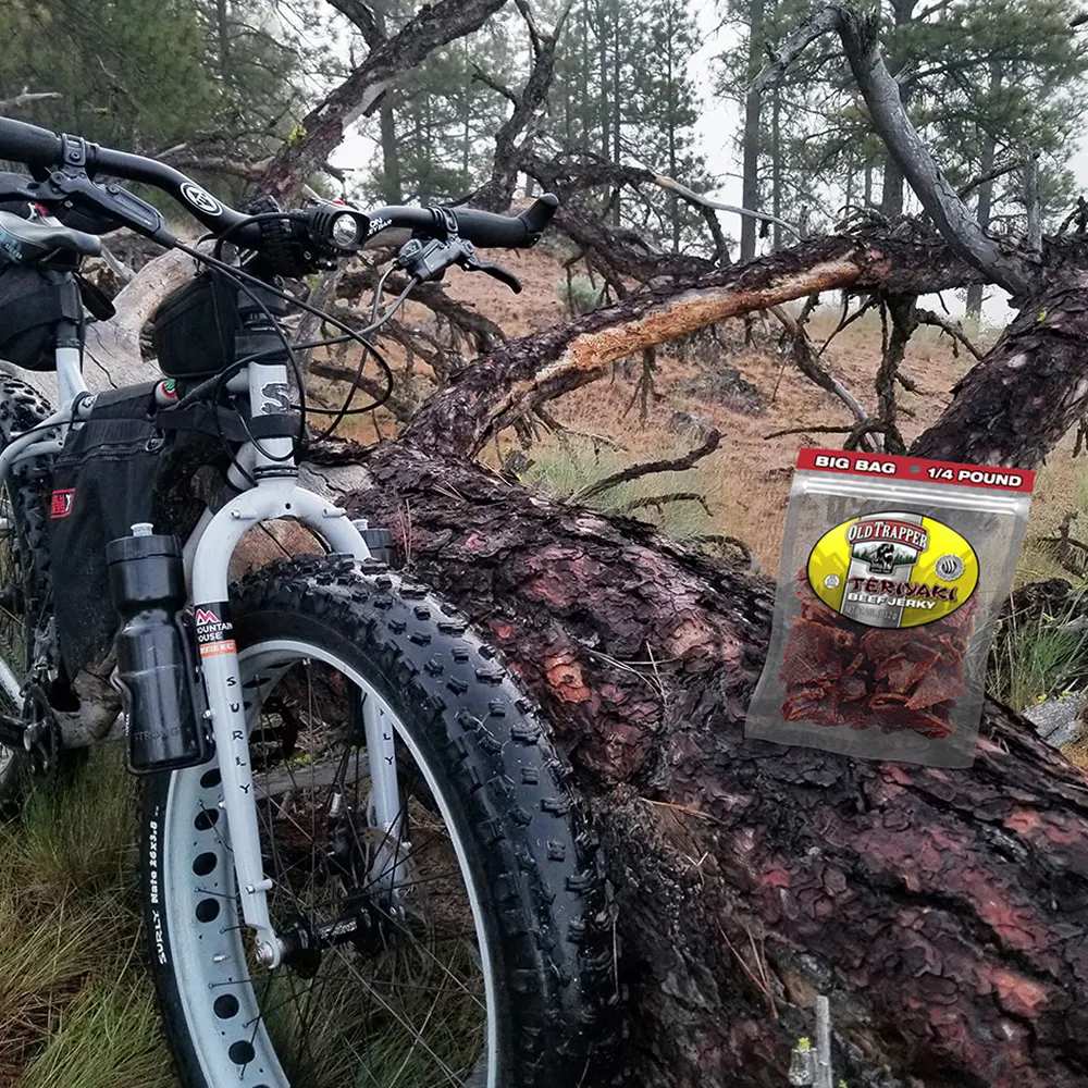 Mountain bike with a bag of Old Trapper's Teriyaki Jerky on a log