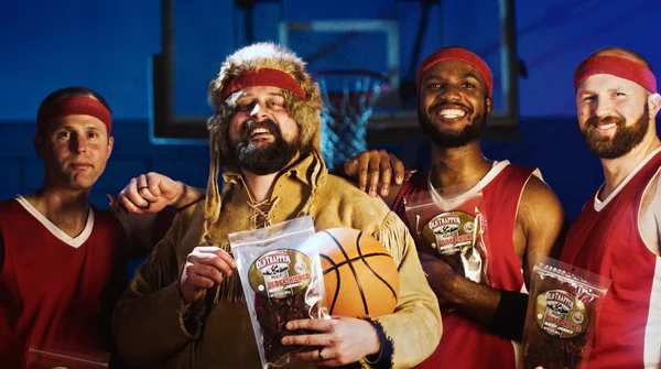 Old Trapper on the basketball court with other players holding bags of jerky