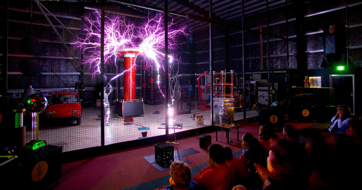 Students watching a spectacular Tesla coil electricity demonstration with purple lightning arcs at Scienceworks museum.