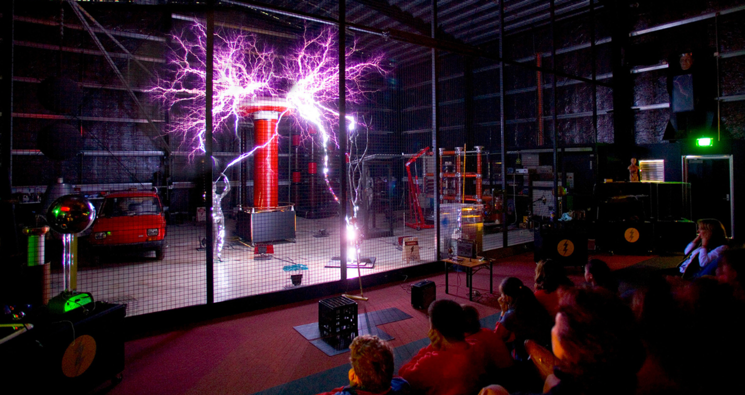 Students watching a spectacular Tesla coil electricity demonstration with purple lightning arcs at Scienceworks museum.