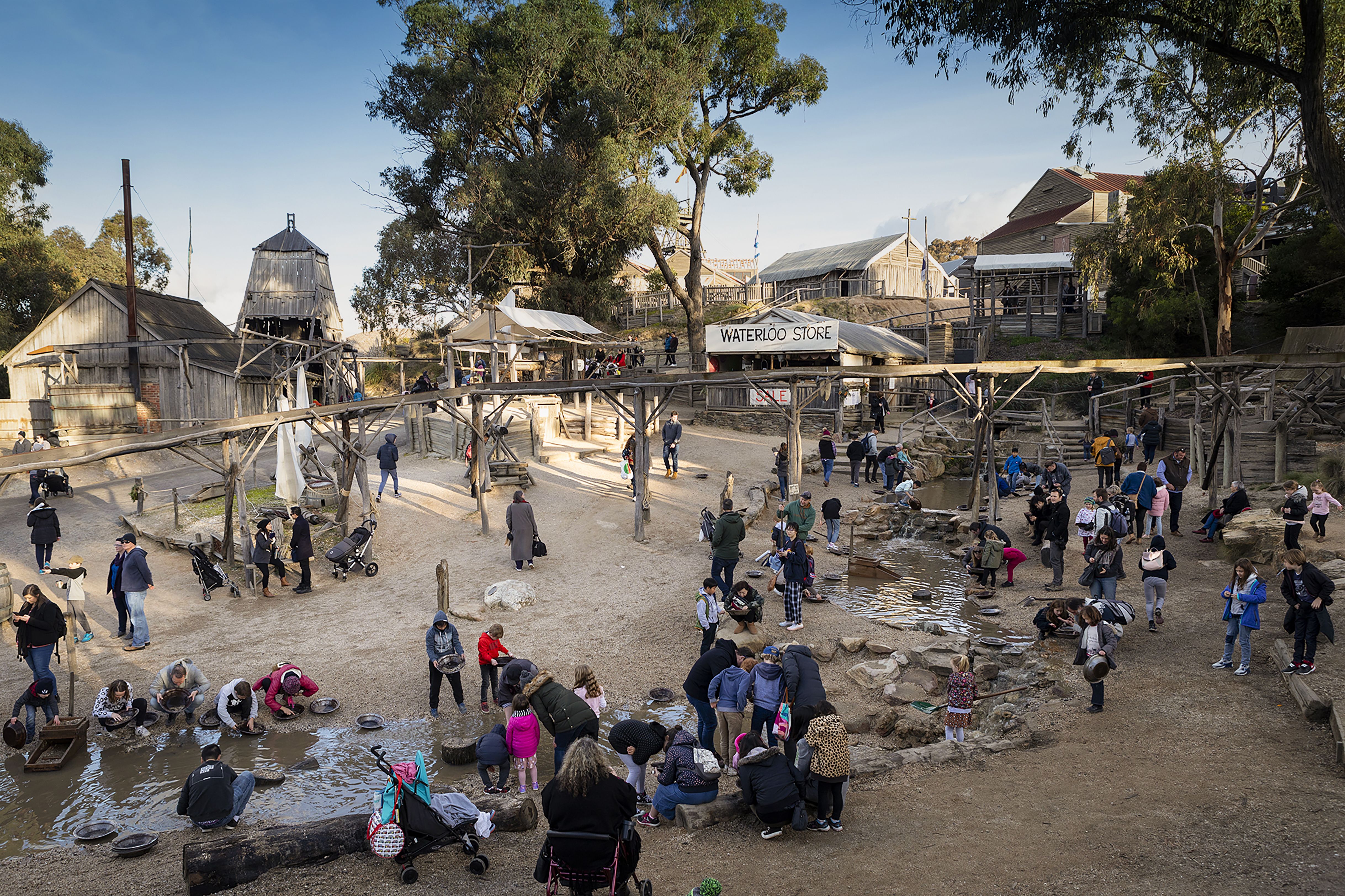 Students panning for gold at Sovereign Hill living museum in Ballarat, with historic buildings and mining structures in the background.