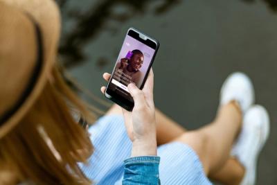 Mulher sentada com chapéu e saia segura o celular na mão e olha o app do Nubank