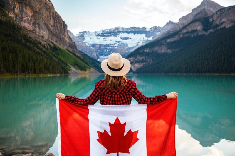Canadian woman holding the Canadian flag in front of a lake and mountain landscape