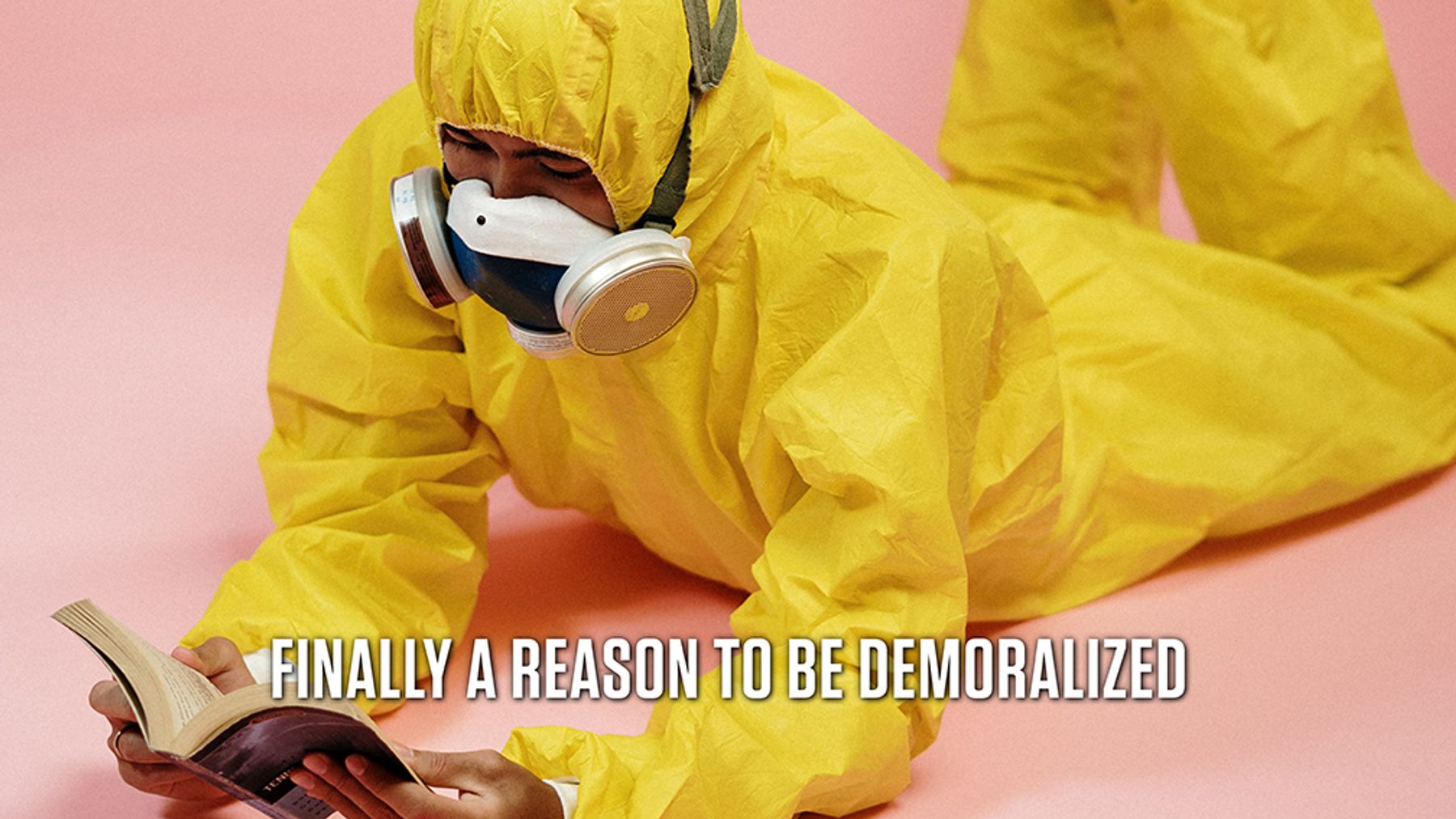 A person in a yellow hazmat suit lies on the floor while reading a book. Text reads: Finally a reason to be demoralized.