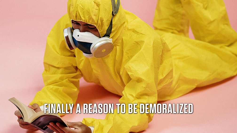 A person in a yellow hazmat suit lies on the floor while reading a book. Text reads: Finally a reason to be demoralized.