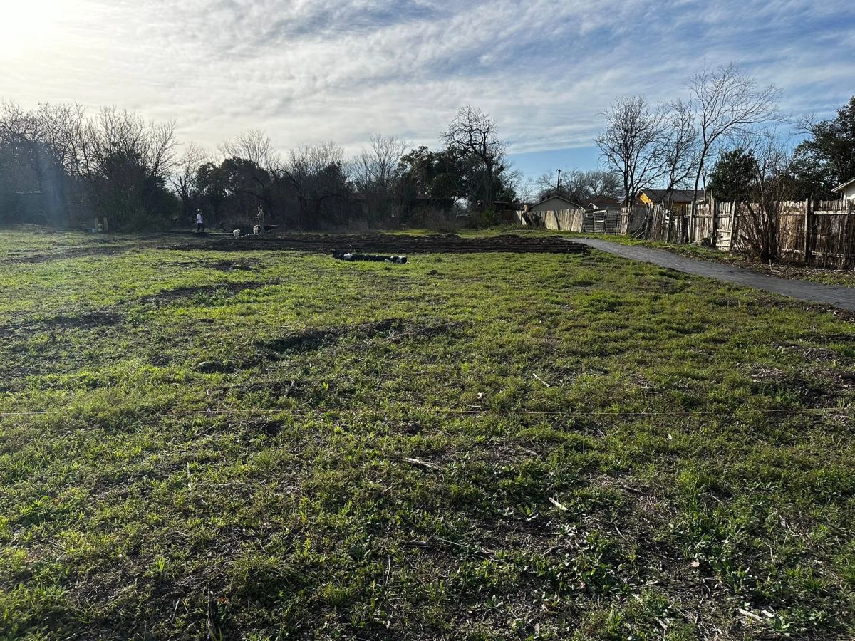 An open stretch of grass on the property under a wide sky, a path and a wooden fence along one side